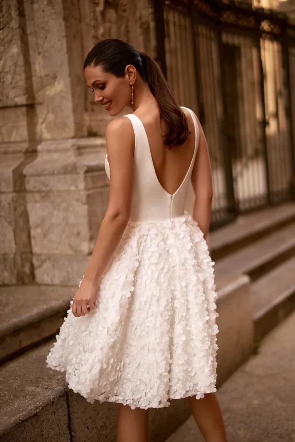 Dos nu en V d'une robe de mariée courte à bretelles larges et jupe à pétales