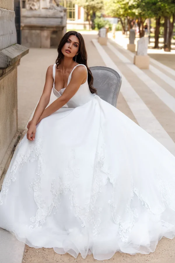 Mariée assise en robe princesse en mikado à col carré et jupe brodée