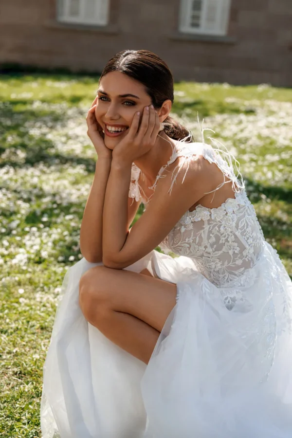 Mariée assise en robe trapèze en tulle à bretelles ornées de plumes