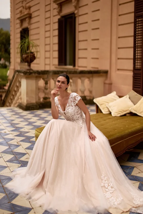 Mariée assise en robe trapèze en tulle nude à mancherons en dentelle